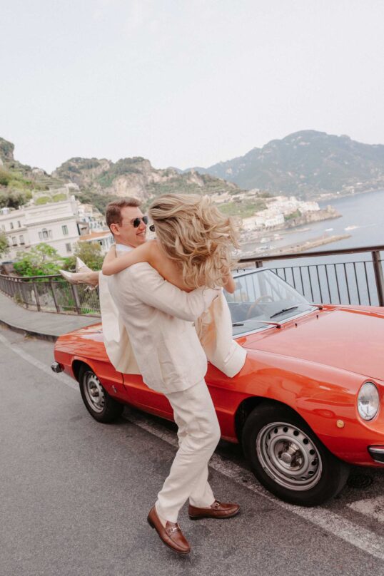 50_JIN_3382 Bride and groom beside a red Positano Vintage car on the Amalfi Coast