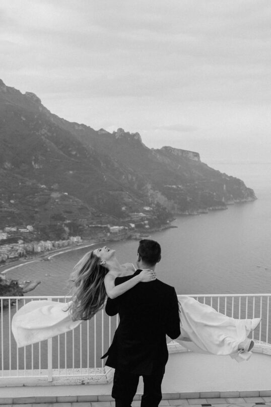 696_JIN_9832 Bride and groom embracing with the Amalfi Coast behind them